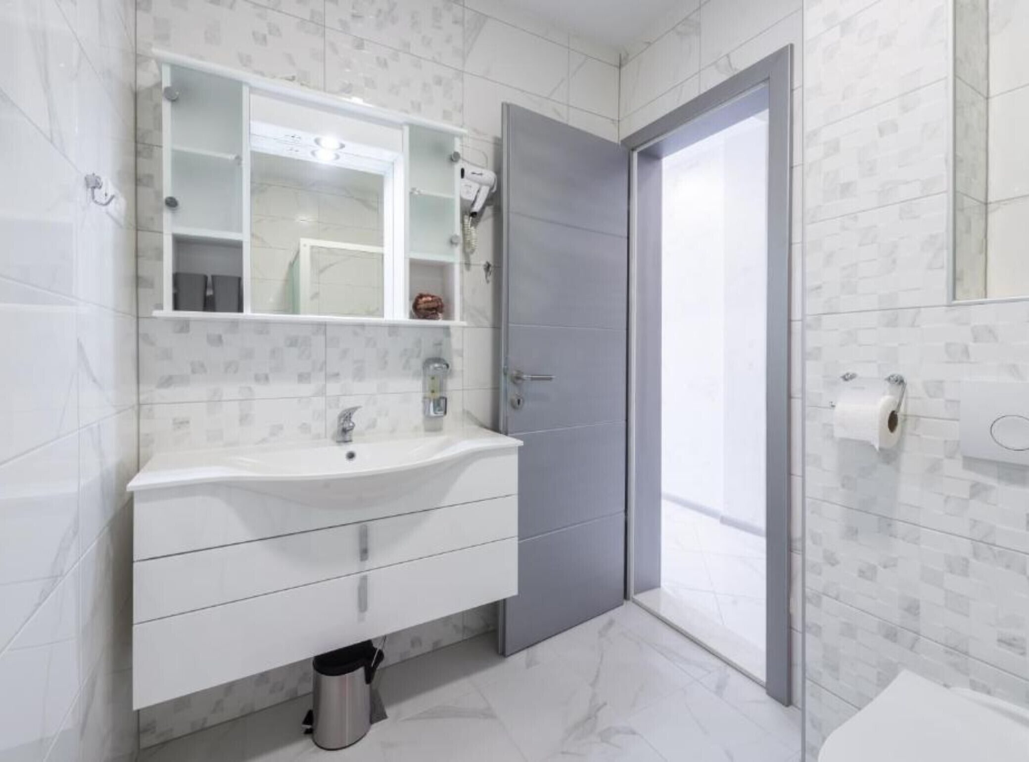 A modern bathroom with a white vanity, a large mirror, a shower area, and a toilet.