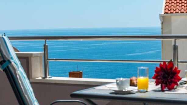 Een balkon met een ontbijtje gedekt, uitzicht op zee en een betegeld dak.