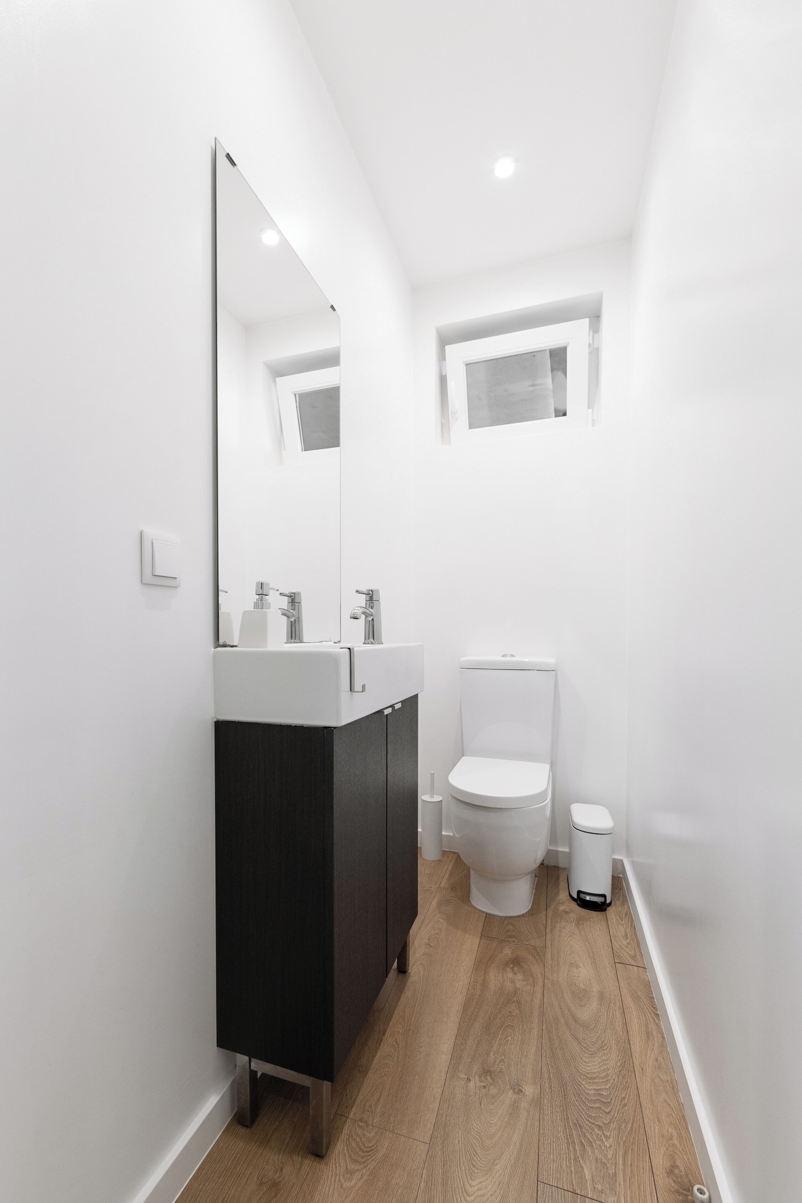 Et moderne badeværelse med en hvid vask, et mørkt skab og et toilet.