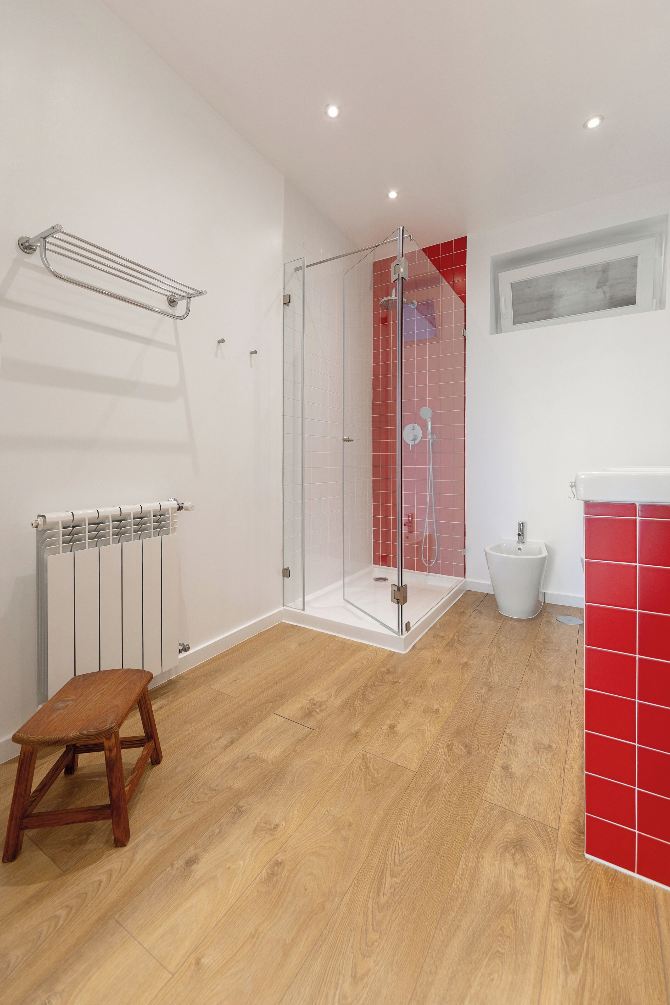 Une salle de bain avec une douche, un radiateur, un tabouret en bois et un mur recouvert de carreaux rouges.