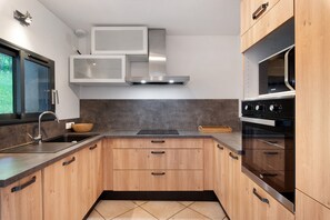 A modern kitchen with a stainless steel range hood, wooden cabinets, a built-in microwave, and a double oven.
