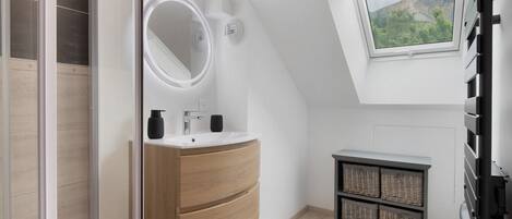 A modern bathroom with a skylight, a round mirror, a sink, and a small cabinet with baskets.