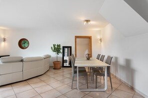 Ein modernes Wohnzimmer mit einer Couch, einem Esstisch mit Stühlen, einer Zimmerpflanze und einem Kamin.