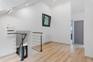 A modern interior with a wooden floor, a black metal railing, a white radiator, and a door leading to another room.
