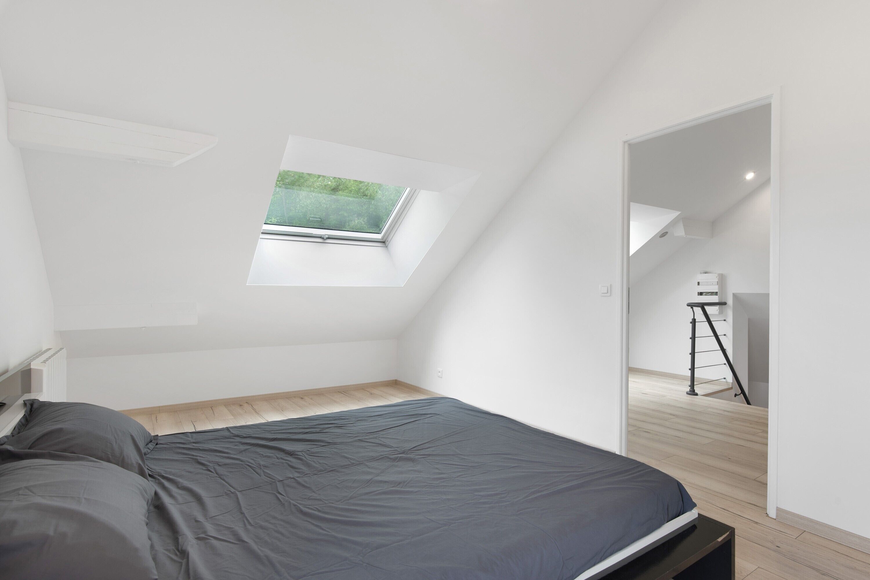 Een slaapkamer met dakraam, een bed en uitzicht op een trap.