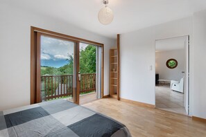 A bedroom with a bed, a wooden floor, a balcony with a view, and a door leading to a bathroom.