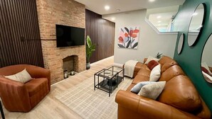 Una sala de estar moderna con chimenea de ladrillo, sofás de cuero, una mesa de centro y un televisor de pantalla plana montado en la pared.