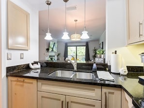 A kitchen with a granite countertop, stainless steel sink, and three pendant lights. - Modern Elegance ~ Excellent Location ~ Steps to the Beach! (Saint Augustine)