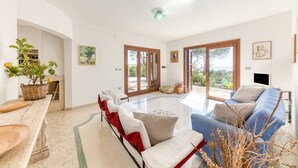 A spacious living area with a sofa, a dining table, and a view through large glass doors. - Nice stone house with sea view & outdoor whirlpool (Patù)
