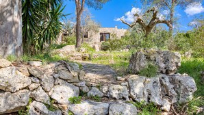 A stone pathway leading to a stone building with a window and door, surrounded by greenery and trees. - Nice stone house with sea view & outdoor whirlpool (Patù)