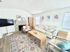 Ein Wohnzimmer mit Flachbildfernseher, einer Couch, einem Couchtisch, einem Kamin und Wandbildern.