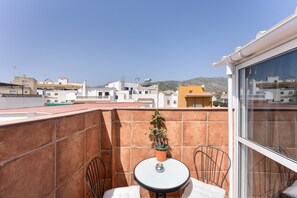 Ein Balkon mit Tisch und Stühlen, einem Blumentopf und Blick auf Gebäude und Hügel.