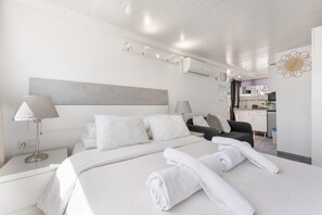 Ein modernes Hotelzimmer mit einem großen Bett, zwei Nachttischen, einem Schreibtisch und einer Küchenzeile im Hintergrund.