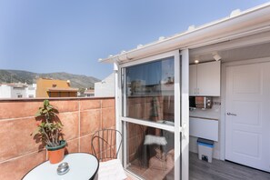 Ein Balkon mit Tisch, Stühlen, einem Blumentopf und einer Schiebetür zu einem Küchenbereich.