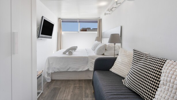 A hotel room with a bed, a sofa, a TV, a window, and an air conditioning unit. - Casa Jose 3 Studio with Sea View and Air Conditioning (Torremolinos)