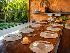 A dining table set with placemats, cutlery, and glasses, with a candle and a star-shaped wall decoration. - Casa Sol do Village Na Praia-PS-BA (Porto Seguro)
