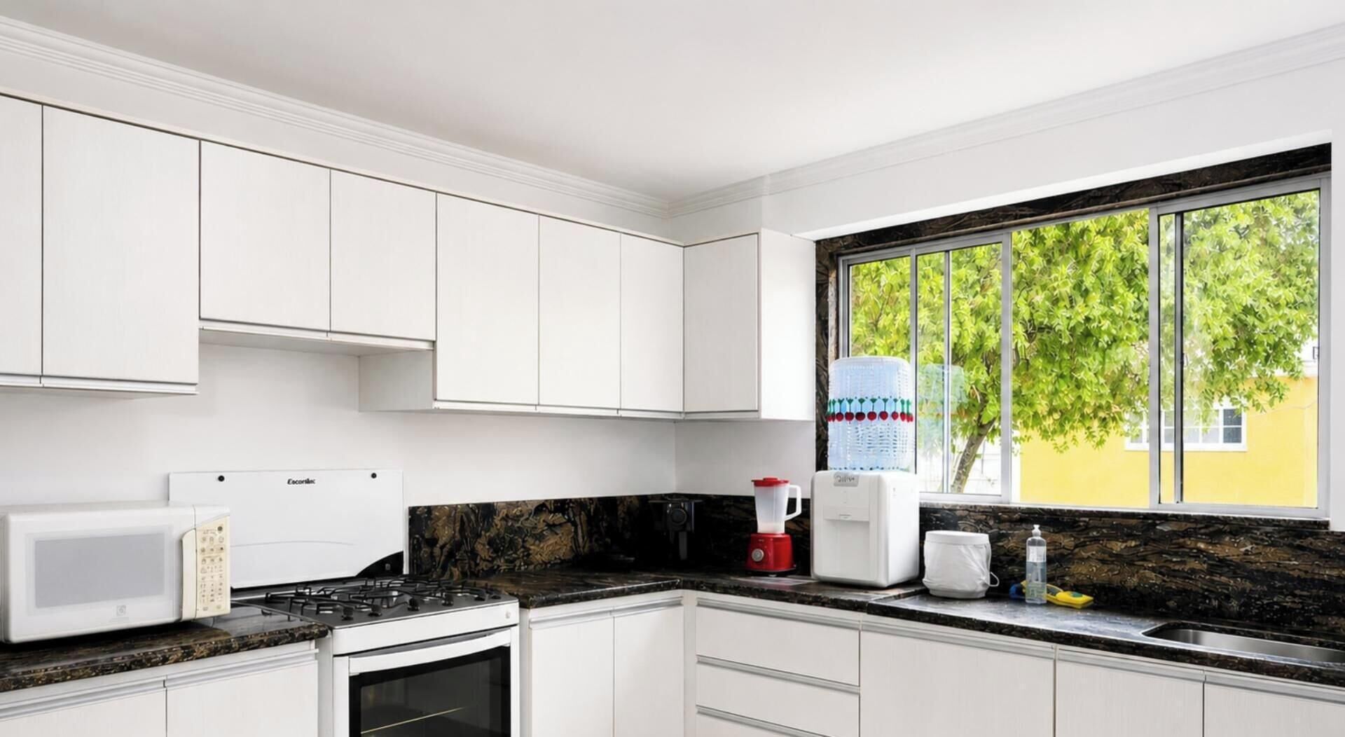 A modern kitchen with white cabinets, a gas stove, a microwave, a coffee maker, and a window with a view of trees.