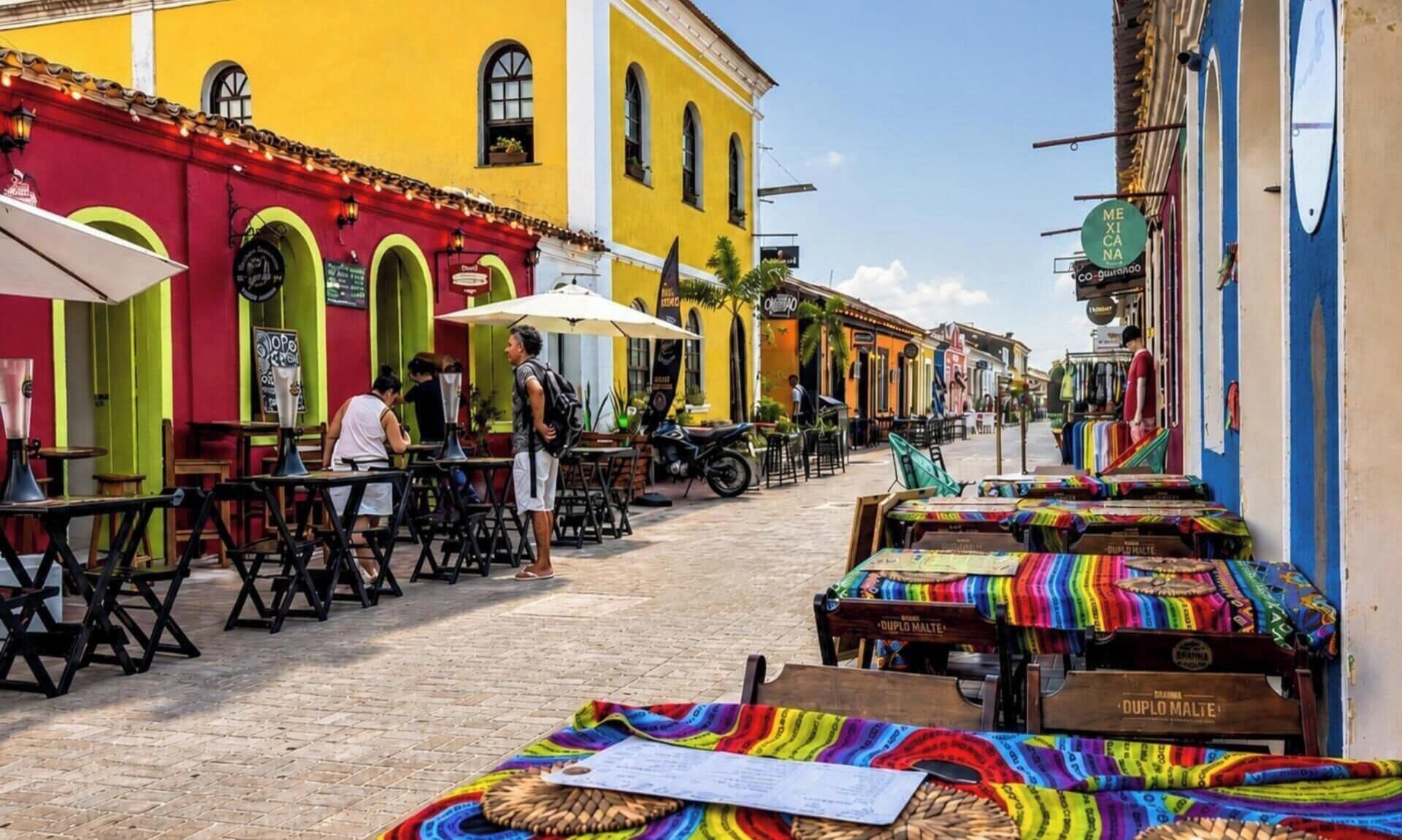 A street with outdoor seating, colorful buildings, and a market stall.