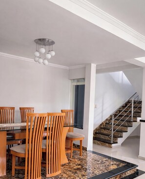 Een eetruimte met een glazen tafel en houten stoelen, een trap met een marmeren afwerking, en een moderne lamp.