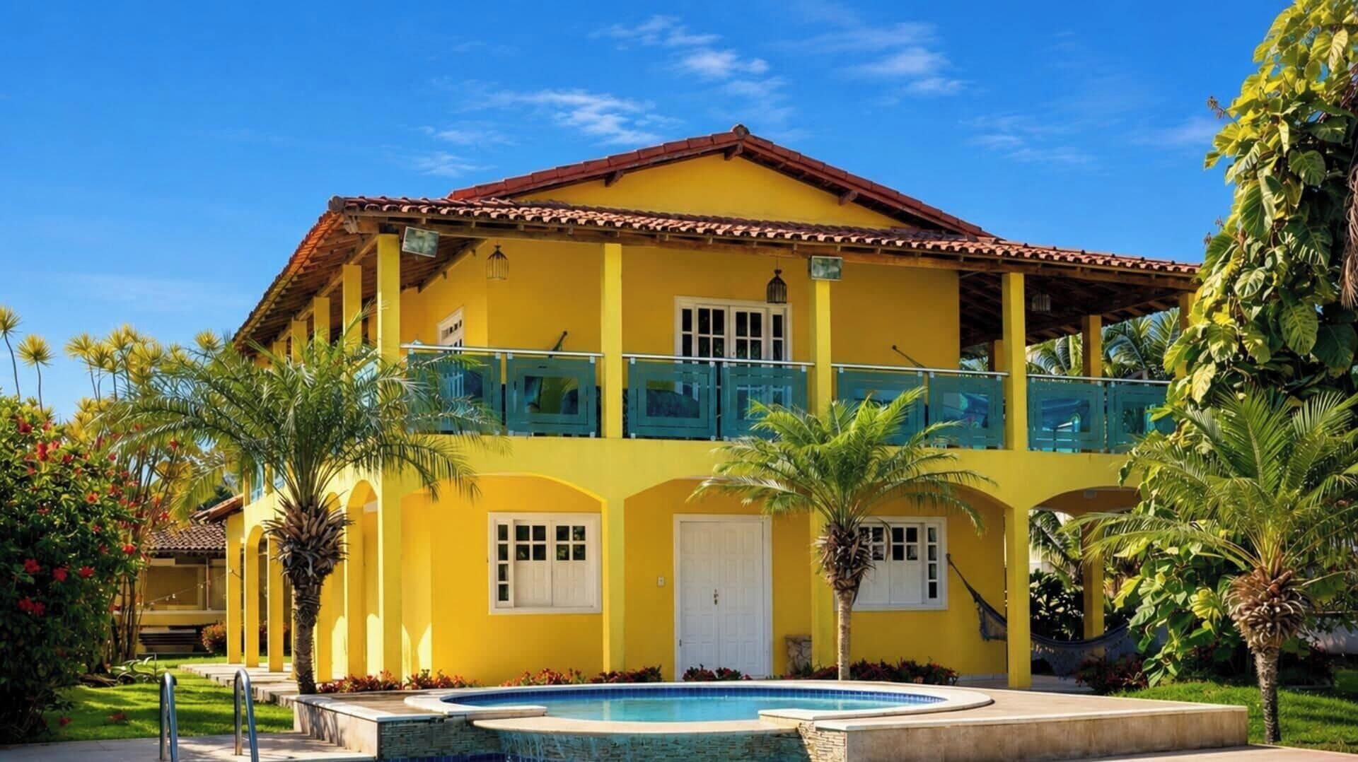 A two-story building with a swimming pool, balconies, and tropical landscaping.