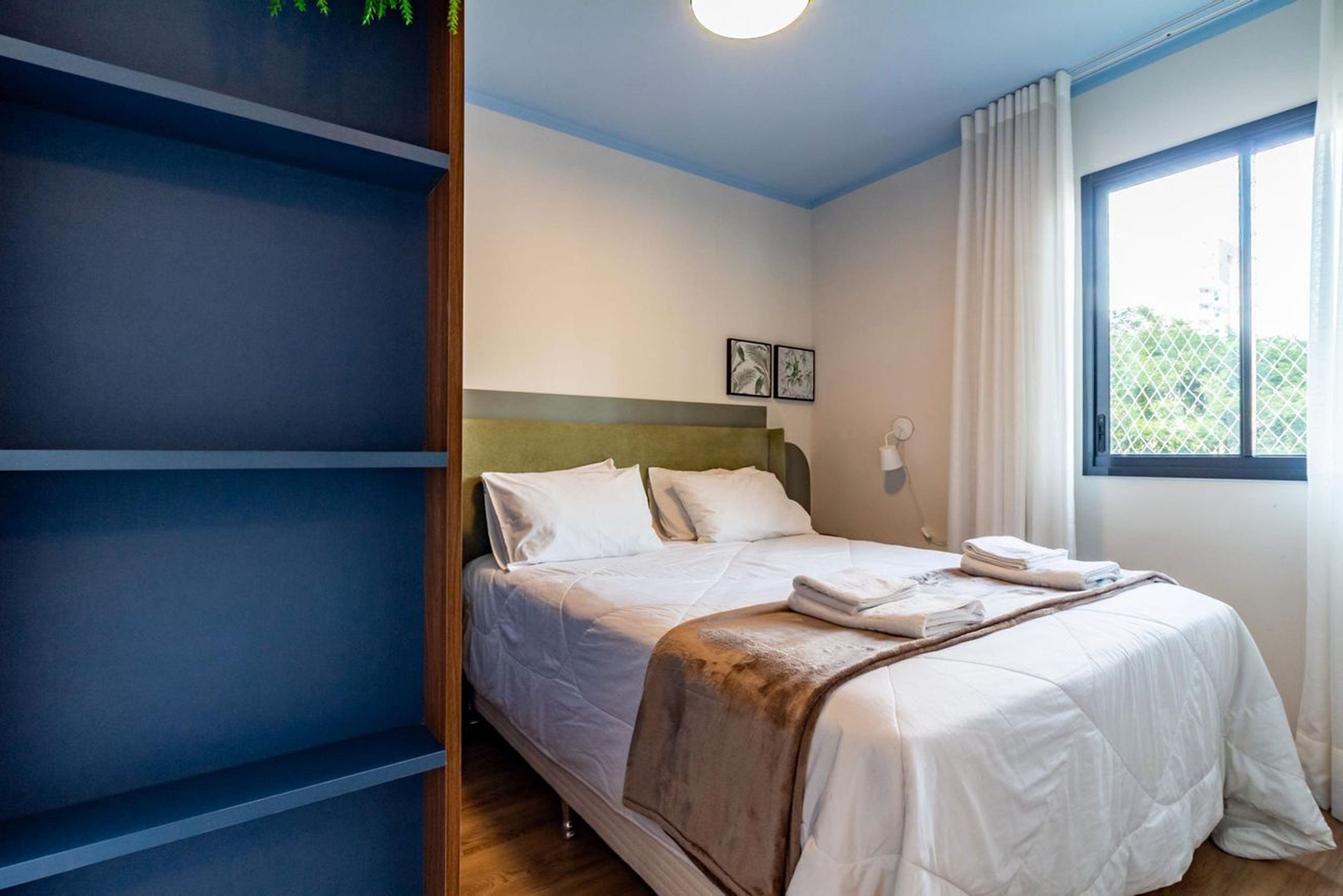 Una camera d'albergo con un letto, una finestra con tende e un lampadario a parete.