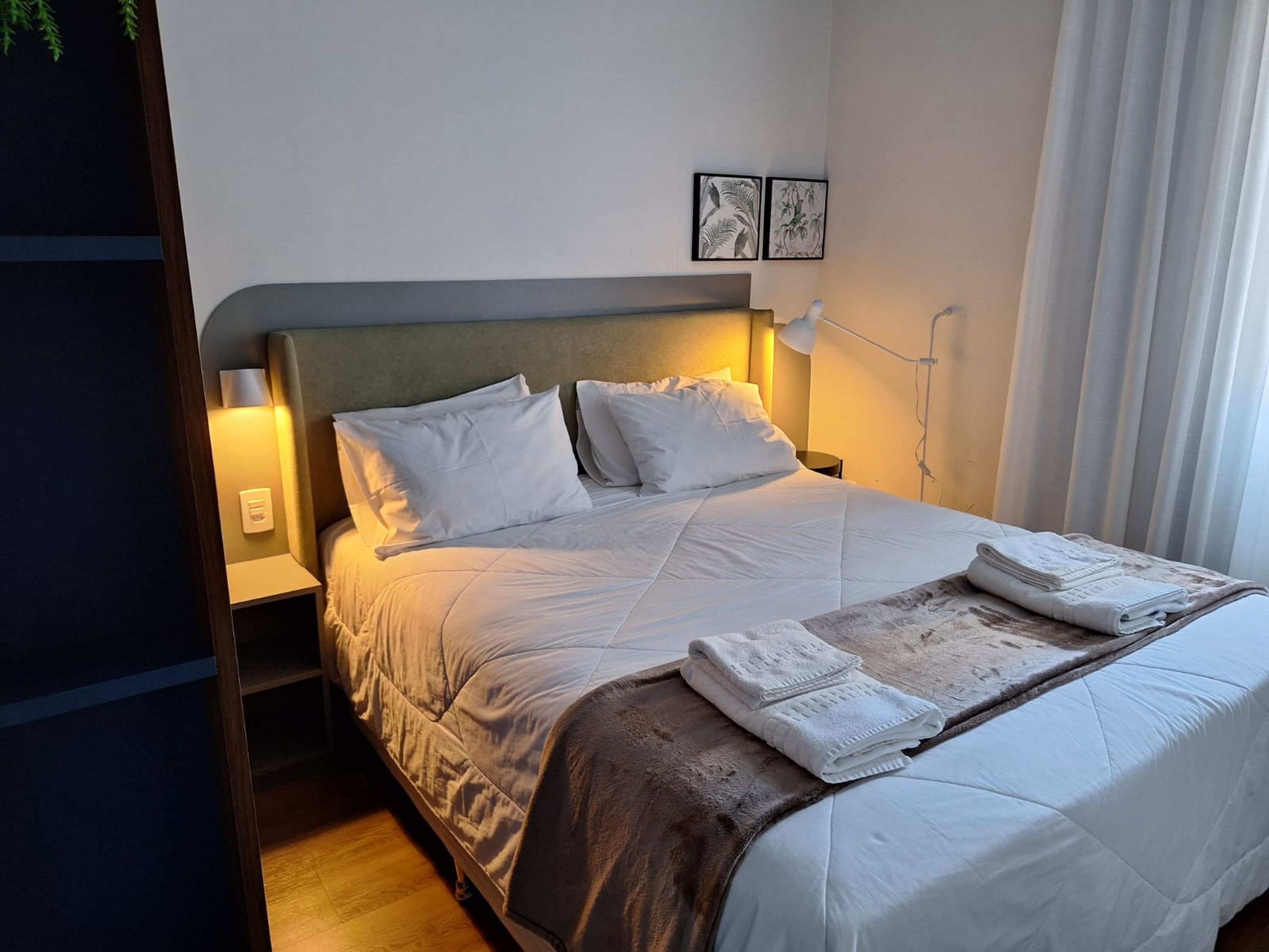 A neatly made bed with white linens, a headboard, and a bedside lamp.