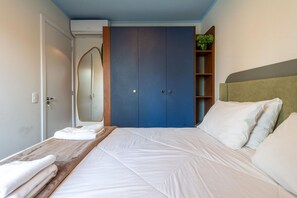 Ein Schlafzimmer mit einem Bett, einem Kleiderschrank, einem Spiegel, einem Regal mit Pflanzen und einem Kopfteil.