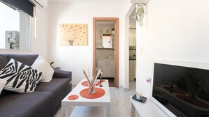 Een moderne woonkamer met een bank, een salontafel, een flatscreen televisie en een keuken op de achtergrond.