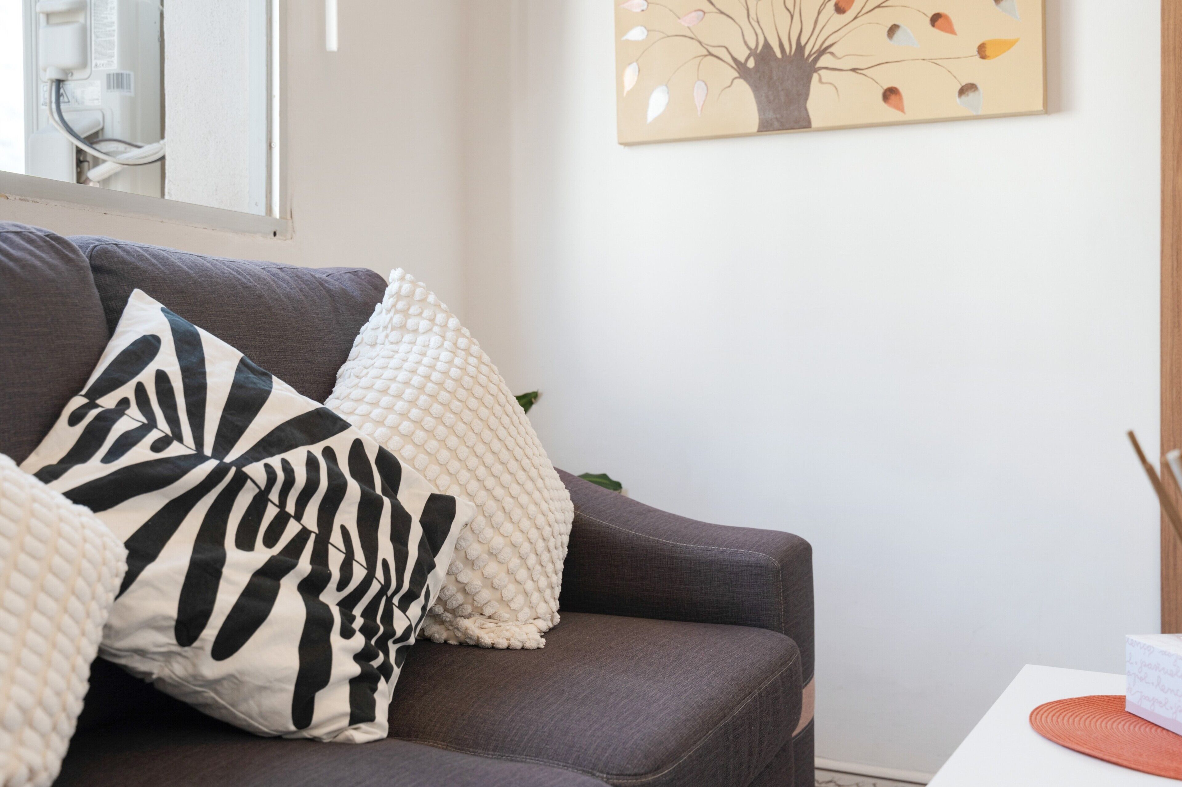 A living room with a grey sofa, a white textured throw blanket, and a wall-mounted painting of a tree.