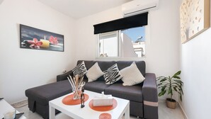 Een moderne woonkamer met een grijze bank, een witte salontafel, een potplant en een schilderij aan de muur.