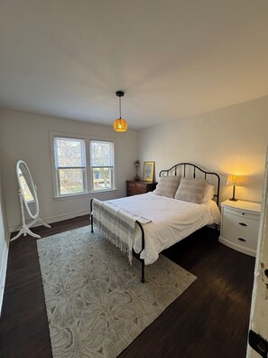 Ein Schlafzimmer mit einem Bett, Nachttischen, einem Spiegel und einem Fenster.