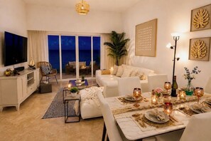 A modern living room with a sofa, dining table set for two, a TV, and a view of the ocean. - OCEANFRONT Punta Palmera Paradise ~ 2 BR apt. in Cap Cana w/Private Beach Access (Punta Cana)