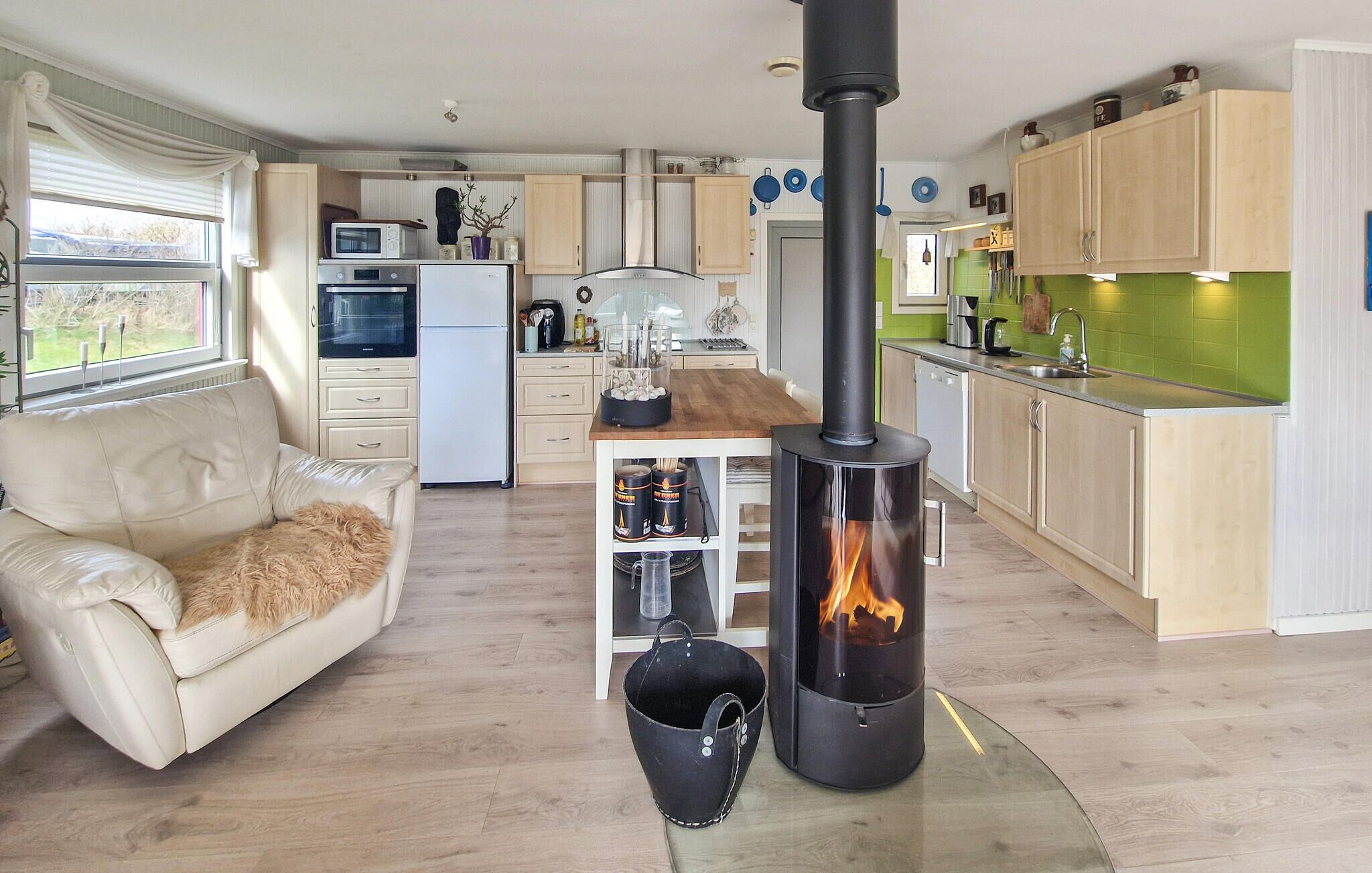 Ein gemütlicher Wohnraum mit Küchenzeile, einer Couch, einem Kamin und Blick ins Freie.