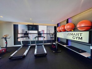 Un gimnasio con cintas de correr, pelotas de ejercicio y una pantalla de televisión.