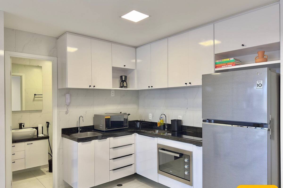 Cozinha moderna com armários brancos, geladeira de aço inoxidável, forno embutido e cafeteira.