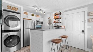 Una cocina compacta con lavadora, refrigerador, microondas y un taburete de bar.