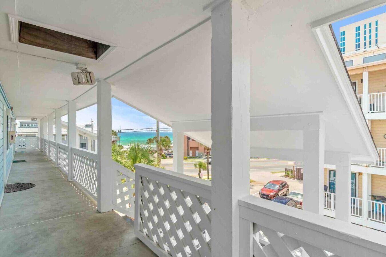 A covered balcony with a view of the beach and ocean, white railings, and a clear sky.