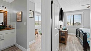 Un baño moderno con un espejo grande, un lavabo y un inodoro. Hay una ventana con persianas y un televisor montado en la pared.