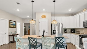 Una cocina moderna con armarios blancos, una isla central con taburetes y luminarias colgantes.