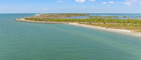 Un paisaje costero con una playa arenosa, aguas tranquilas y una barrera rocosa.