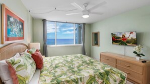 A bedroom with a bed, a ceiling fan, a window with a view, a dresser, and a TV. - Oceanfront A/C 1BR GEM ~ Whales, Dolphins & Sunsets (Kailua-Kona)