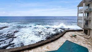 A pool with a view of the ocean, a stone deck, and a building with a balcony. - Oceanfront A/C 1BR GEM ~ Whales, Dolphins & Sunsets (Kailua-Kona)