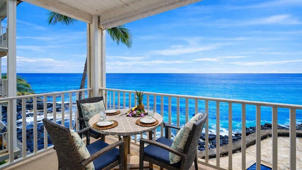 A balcony with a table set for two, overlooking a beach with the ocean. - Oceanfront A/C 1BR GEM ~ Whales, Dolphins & Sunsets (Kailua-Kona)