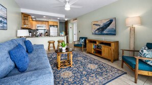 A living room with a sofa, a coffee table, a rug, a TV stand, and a chair. - Oceanfront A/C 1BR GEM ~ Whales, Dolphins & Sunsets (Kailua-Kona)