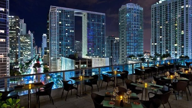 A rooftop bar with tables and chairs, overlooking a cityscape with high-rise buildings. - Deluxe Brickell Suite w/ pool, gym, & city views! (Miami)
