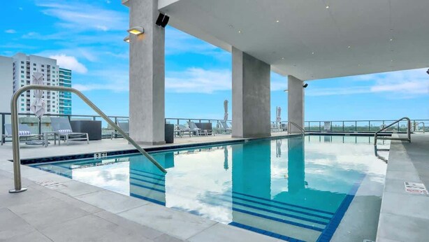 Una piscina interior con agua azul cristalina, pilares de hormigón y vistas al horizonte de la ciudad.