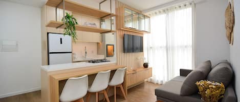 Una cocina moderna con un refrigerador empotrado, un comedor con sillas, un sofá gris y una mesita auxiliar con un jarrón.
