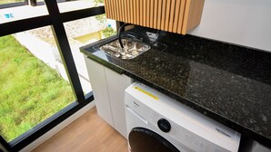 Uma cozinha com máquina de lavar, pia e janela com vista para um gramado.