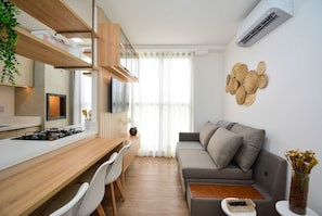 Una cocina moderna con encimera de madera, sillas blancas, un sofá gris y un aire acondicionado instalado en la pared.