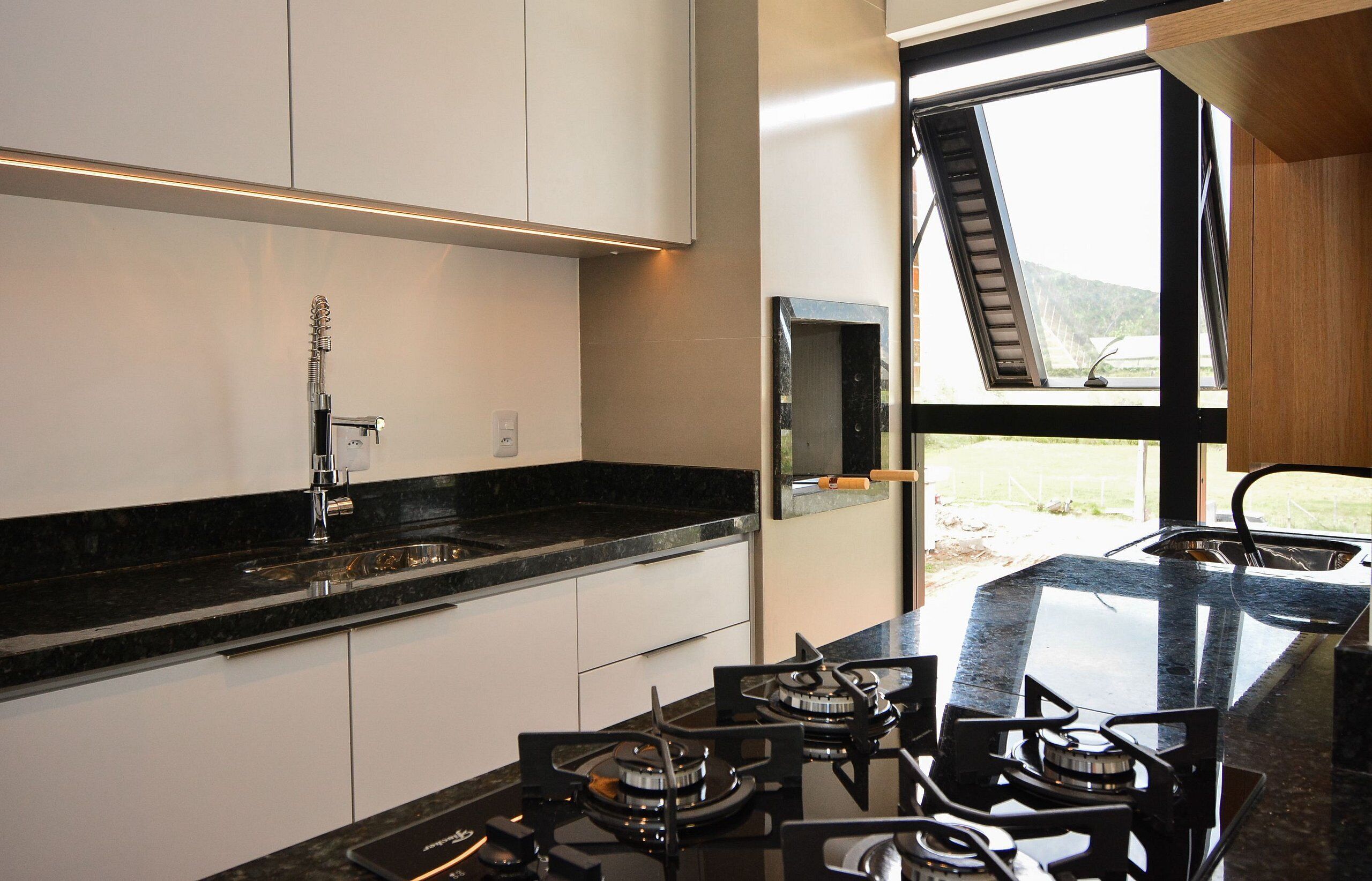 Een moderne keuken met een gasfornuis, een spoelbak en een raam met uitzicht op de omgeving.